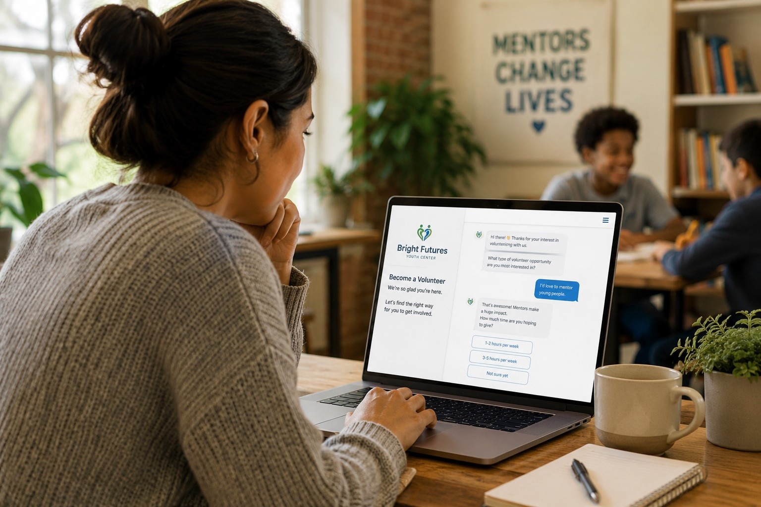 A prospective volunteer uses a laptop with a conversational volunteer intake form while youth program activity happens softly in the background.
